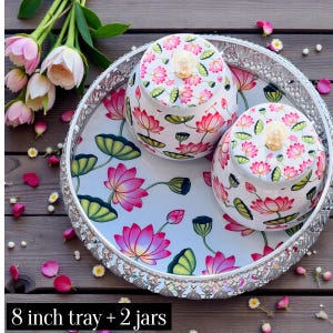 May include: A round 8 inch silver-toned metal tray with a decorative filigree edge, featuring two matching lidded jars. The tray and jars are decorated with a white background and a colorful pattern of pink lotus flowers and green leaves.