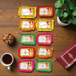 May include: A collection of colorful, rectangular photo frames with decorative trim. Each frame features a portrait of a woman and is adorned with small, sparkling embellishments. The frames are arranged on a wooden surface.