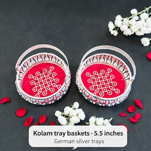 May include: Two German silver tray baskets, each with a red interior and a white geometric design. The baskets have silver handles and measure 5.5 inches in diameter. White flowers and red petals are scattered around the baskets.