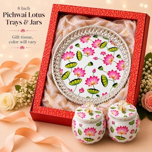 May include: An 8 inch round tray with a silver-toned decorative rim and a white surface featuring a pink and green lotus flower pattern, accompanied by two matching lidded jars with clear crystal-like knobs, all presented in a red gift box.