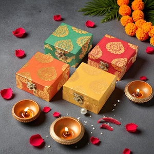 Peut inclure: Quatre boîtes carrées colorées, ornées de motifs dorés et de fermoirs en métal. Les boîtes sont vertes, rouges, orange et jaunes. De petites bougies allumées dans des bols dorés et des pétales de rose sont disposées autour.