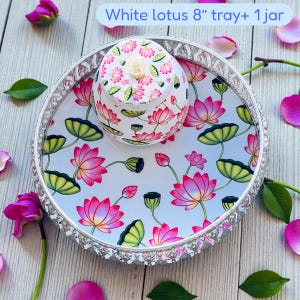 May include: A round 8-inch silver-toned tray featuring a white surface with a pink lotus flower and green leaf pattern, accompanied by a matching lidded jar with the same floral design. The text White lotus 8&rdquo; tray+ 1 jar is visible.