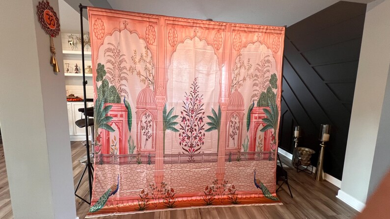 May include: A large rectangular fabric backdrop featuring a printed architectural scene with peach and pink arches, green palm trees, and floral motifs. The design includes a low railing, two peacocks at the base, and a central flowering plant.