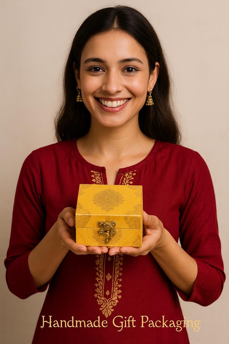 May include: A smiling person holds a yellow gift box with a decorative pattern and a metal clasp. The box is labeled "Handmade Gift Packaging" in gold lettering. The person is wearing a red top.