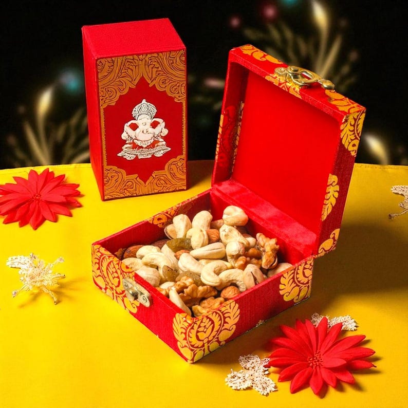 May include: A red box with gold decorative accents and a hinged lid, filled with mixed nuts. A smaller matching box is visible in the background. The boxes are on a yellow surface, with red flower decorations.