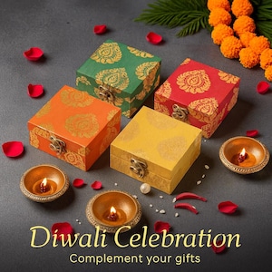 May include: Four colorful square boxes with gold floral patterns and metal clasps are arranged with lit candles in small bowls, rose petals, and marigold flowers. The text "Diwali Celebration" and "Complement your gifts" are at the bottom.
