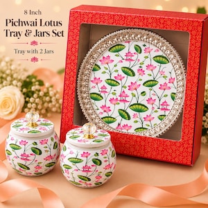 May include: An 8-inch Pichwai Lotus tray and two jars set featuring a white surface with a repeating pink lotus flower and green leaf pattern. The round tray has a metallic beaded rim, and both jars include matching lids with clear crystal knobs.