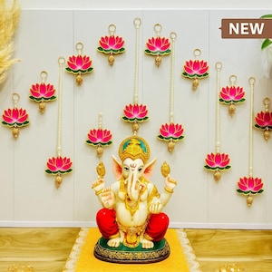 May include: Wall decor featuring pink lotus flower ornaments with gold accents and pearl strands. A statue of a deity sits below the hanging decorations. The text "Lotus Pearl Hanging Wall Decor" is displayed at the top and bottom of the image.