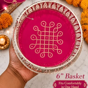 May include: A round magenta pink basket with a silver-toned rim featuring an embossed pattern. The center of the basket displays a gold-colored geometric Kolam design. The text on the image includes Color: Magenta Pink, 6" Basket, and Fits Comfortably in One Hand.