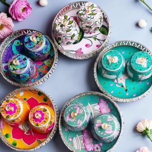 May include: Five circular silver-toned metal trays, each containing two matching lidded jars. The sets feature vibrant, multi-colored floral, peacock, and animal motifs, with clear crystal-like knobs on each lid, arranged in a circular pattern.
