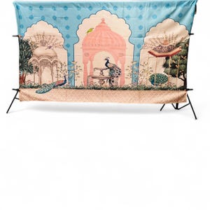 May include: A rectangular fabric backdrop featuring a light blue sky background with a repeating diamond pattern. The design displays three arched structures, including a central pink pavilion with a fountain, peacocks, and lush greenery.