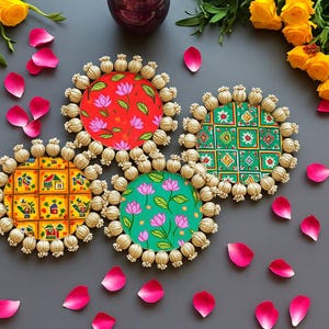 May include: Four colorful, round coasters with intricate designs. Each coaster features a different pattern: a red floral print, a green floral print, a yellow house print, and a green geometric print. The coasters are surrounded by a beige trim and pink rose petals.