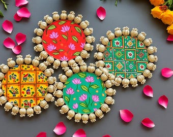 May include: Four decorative coasters with colorful floral and geometric patterns. Each coaster has a circular design with a patterned fabric center and a beaded border. Pink rose petals and yellow roses are scattered around the coasters on a gray surface.