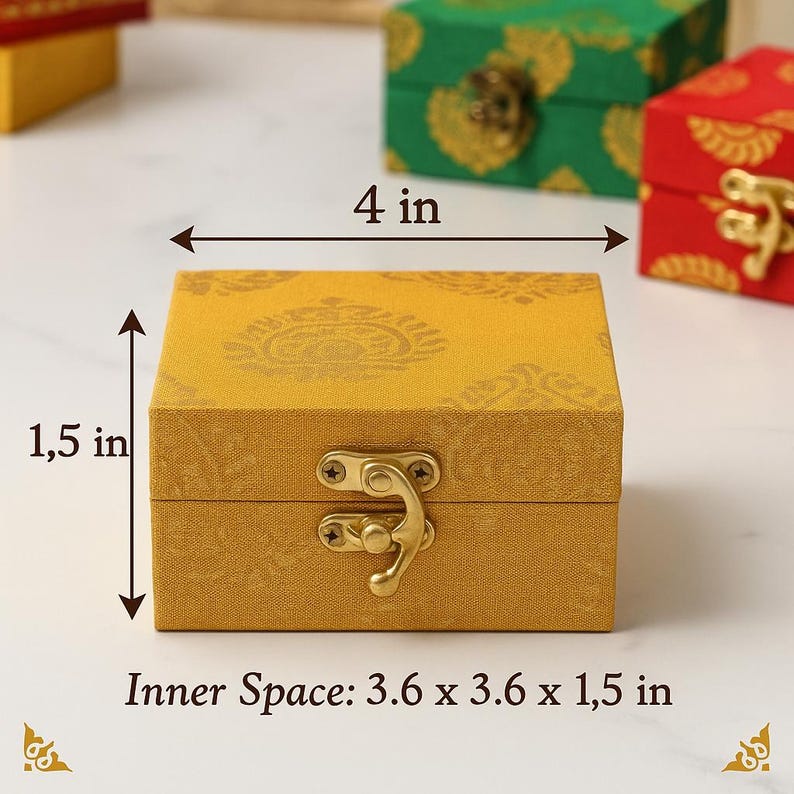 May include: A mustard-yellow square box with a gold clasp, measuring 4 inches wide and 1.5 inches high. The box has a patterned design and is displayed with other decorative boxes. The inner space is 3.6 x 3.6 x 1.5 inches.