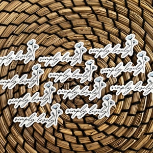 Puede incluir: Un conjunto de 12 pegatinas blancas con el texto "simply lovely" en letra negra. Cada pegatina presenta una pequeña ilustración de flor azul.