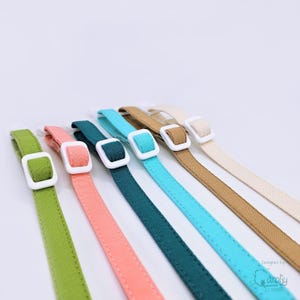 May include: A set of six fabric straps in various colors including lime green, coral, dark teal, bright blue, tan, and cream. Each strap features a white rectangular plastic sliding buckle for adjustment, with visible stitching along the edges.