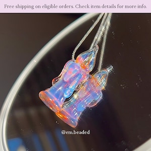 K&ouml;nnte beinhalten: Zwei Glas-Anh&auml;nger-Halsketten mit schillernden Farben in Blau, Orange und Rosa. Die Anh&auml;nger sind wie stilisierte Flammen geformt und h&auml;ngen an filigranen Silberketten. Das Bild enth&auml;lt den Text "@em.beaded".