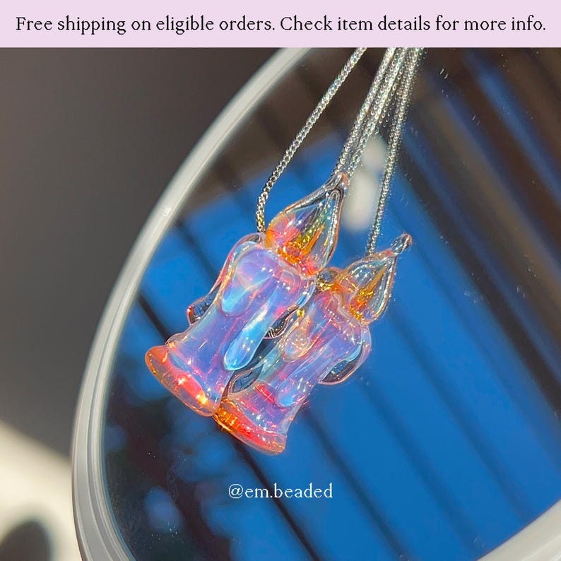 K&ouml;nnte beinhalten: Zwei Halsketten mit Anh&auml;ngern aus schillerndem Glas. Jeder Anh&auml;nger hat eine einzigartige Form mit einer Mischung aus Farben, darunter Orange, Rosa und Blau. Die Halsketten h&auml;ngen an filigranen Silberketten. Das Bild enth&auml;lt den Text "@em.beaded".