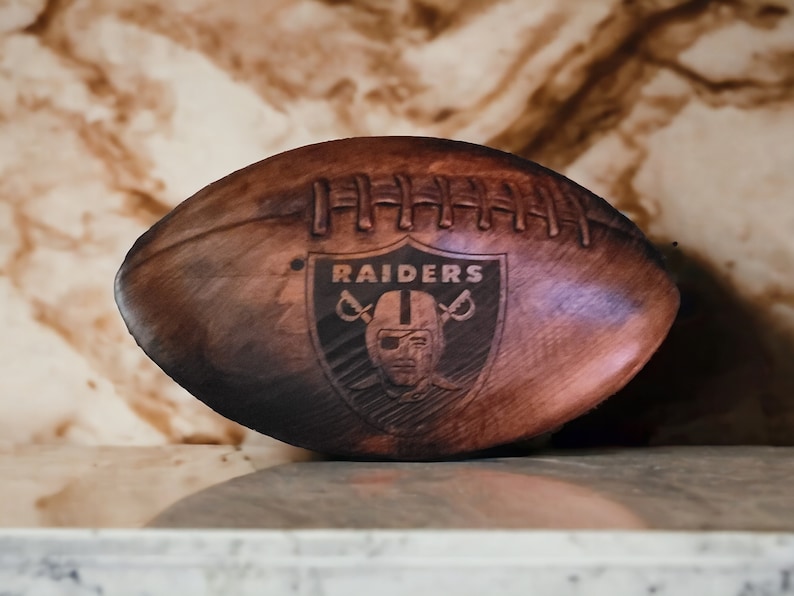 May include: A brown leather football with the word "RAIDERS" and a skull and crossbones logo.