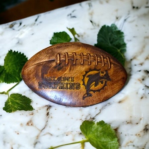 May include: A wooden football with the Miami Dolphins logo and the words "Miami Dolphins" engraved on it.