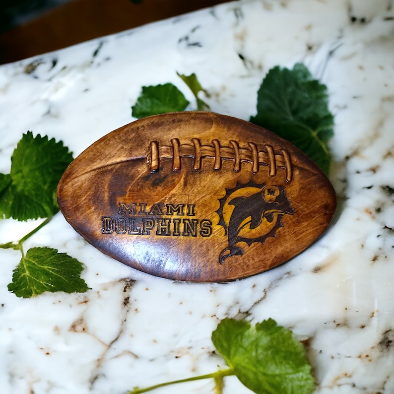 May include: A wooden football with the Miami Dolphins logo and the words "Miami Dolphins" engraved on it.