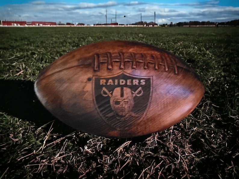 May include: A brown wooden football with the Raiders logo and the word "RAIDERS" in white lettering.