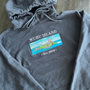 Puede incluir: Sudadera con capucha negra con una imagen bordada en blanco de una isla con el texto "WUHU ISLAND . Est. 2009."