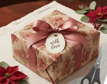May include: A wrapped gift box with floral patterned paper and a mauve ribbon tied in a bow. A tag that says "with love" hangs from the bow. Scissors and a poinsettia are nearby.