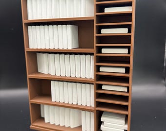 May include: A brown miniature bookshelf with multiple shelves filled with stacks of white books. The bookshelf also has a vertical section with smaller shelves holding individual white items. The design is simple and clean, suitable for a dollhouse or miniature setting.