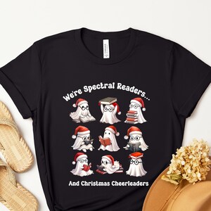 May include: Black t-shirt with a design of cartoon ghosts in Santa hats, reading books. The text says "We're Spectral Readers... And Christmas Cheerleaders."