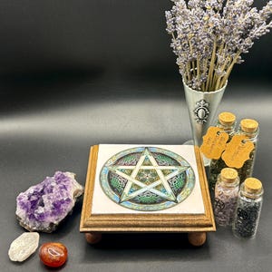 May include: A wooden stand with a tile featuring a pentagram design. The stand is surrounded by crystals, small glass jars with cork stoppers, and a metal cone filled with lavender. The tile has green, blue, and gold accents.