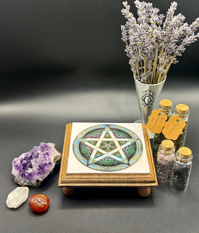 May include: A wooden stand with a tile featuring a pentagram design. The stand is surrounded by crystals, small glass jars with cork stoppers, and a metal cone filled with lavender. The tile has green, blue, and gold accents.