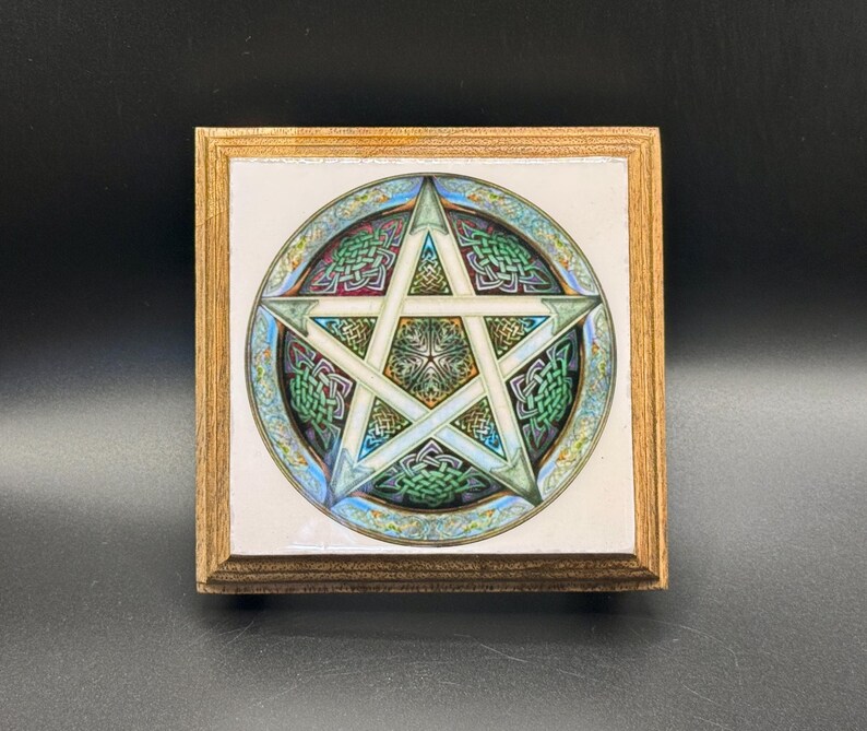May include: A square wooden plaque featuring a pentagram design. The pentagram is set within a circular border with Celtic knot patterns in green, blue, and white. The wooden frame has a light brown finish.