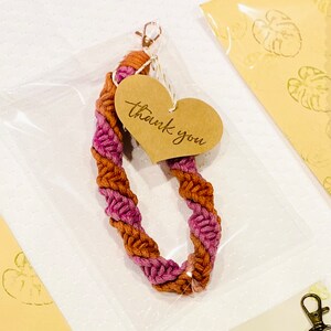 May include: A pink and brown braided cord keychain with a heart-shaped tag that says "thank you".