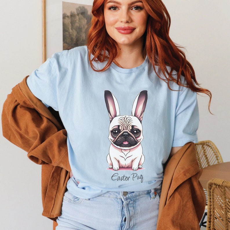 May include: A light blue t-shirt featuring a cartoon image of a pug wearing bunny ears. The text "Easter Pug" is printed below the image.