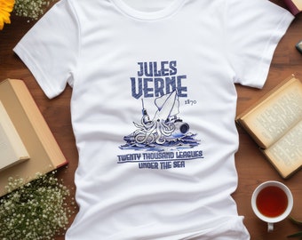 Puede incluir: Camiseta blanca con un gráfico azul de un calamar atacando un submarino. El gráfico incluye el texto "Jules Verne 1870 Veinte mil leguas de viaje submarino".