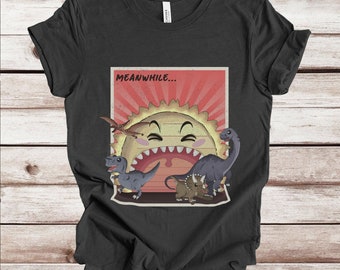 May include: A black t-shirt with a retro-style graphic of a cartoon sun with a wide open mouth and dinosaurs surrounding it. The text "MEANWHILE..." is above the sun.