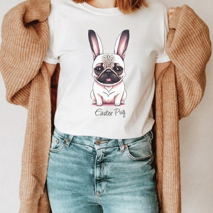 May include: White t-shirt featuring a cartoon image of a pug wearing bunny ears. The text "Easter Pug" is printed below the image.