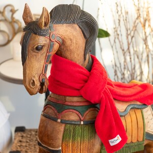 May include: A wooden rocking horse with a red scarf around its neck. The horse is painted with colourful details and has a saddle.