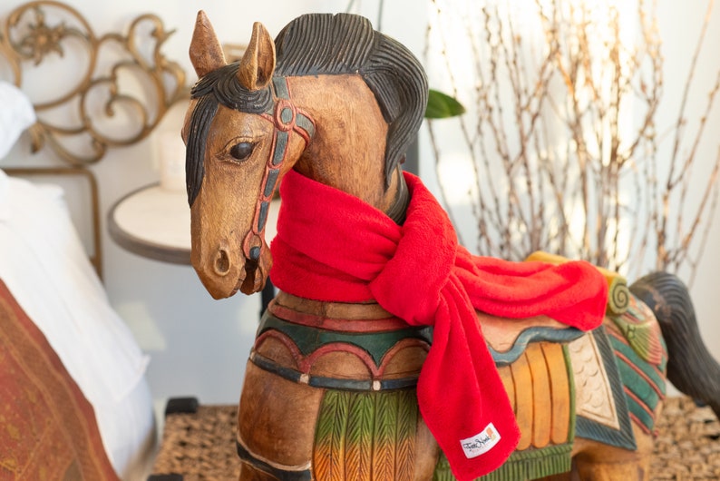 May include: A wooden rocking horse with a red scarf around its neck. The horse is painted with colourful details and has a saddle.