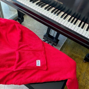 May include: A red microfiber cleaning cloth with a small pocket on the side. The cloth is folded and draped over a black piano with the text "STEINWAY & SONS" on the side.