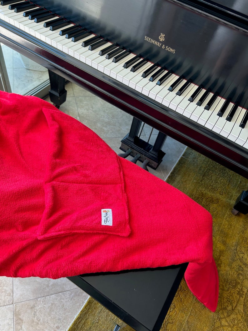 May include: A red microfiber cleaning cloth with a small pocket on the side. The cloth is folded and draped over a black piano with the text "STEINWAY & SONS" on the side.