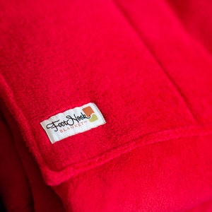 May include: A red fleece blanket with a white tag that says "Foot Nook Blanket" in black cursive lettering.