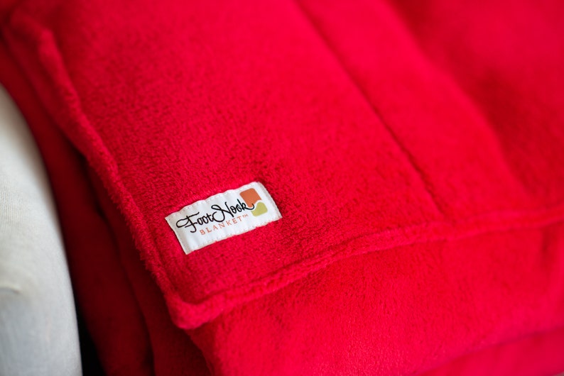 May include: A red fleece blanket with a white tag that says "Foot Nook Blanket" in black cursive lettering.