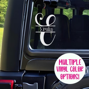May include: White vinyl decal with a cursive letter "E" and the name "Emily" below it. The decal is on the back window of a black car. The text "MULTIPLE VINYL COLOR OPTIONS!" is on a white circle.