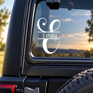 May include: A white vinyl decal applied to a vehicle window, featuring a large stylized letter E with a split design. The name Emily is written in a cursive script font within the horizontal split section of the letter.