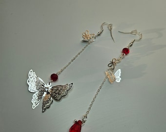 May include: A pair of silver dangle earrings with red and white butterfly charms. The earrings feature a red crystal bead and a silver butterfly charm.