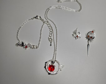 May include: A silver necklace with a red glass pendant in the shape of a circle with floral accents. The necklace comes with a matching bracelet and a pair of earrings with red and silver accents.