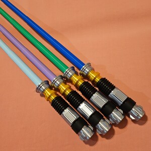 May include: Five lightsaber toys in various colors, including blue, green, purple, and light blue. The lightsabers are silver and gold with black handles.