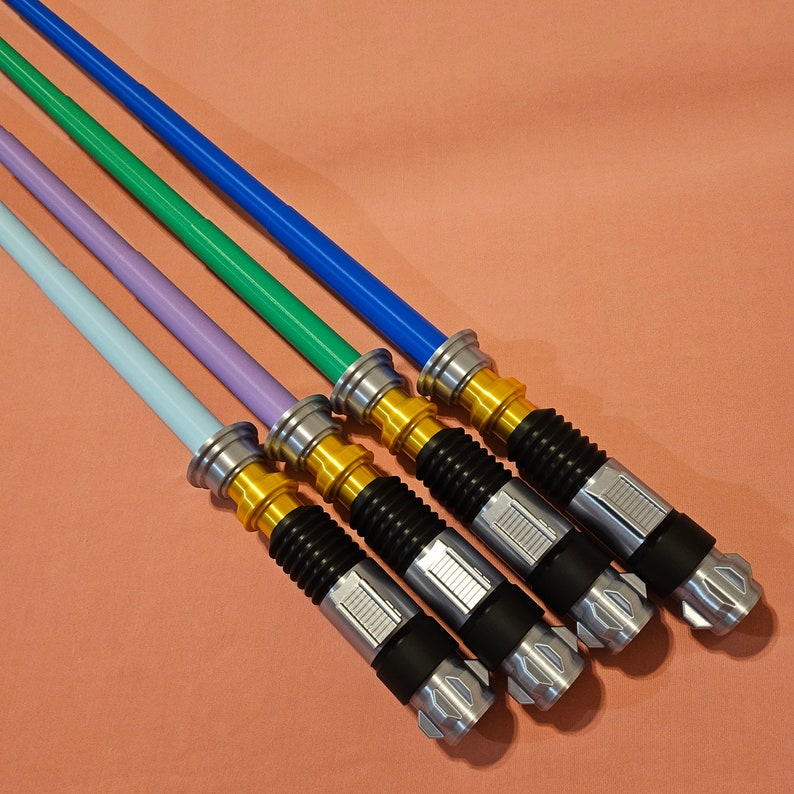 May include: Five lightsaber toys in various colors, including blue, green, purple, and light blue. The lightsabers are silver and gold with black handles.